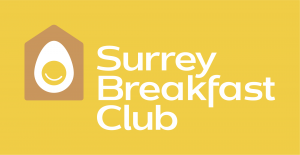 The Surrey Breakfast Club logo has white text on a mustard yellow background. Beside the words is a house with an egg inside.