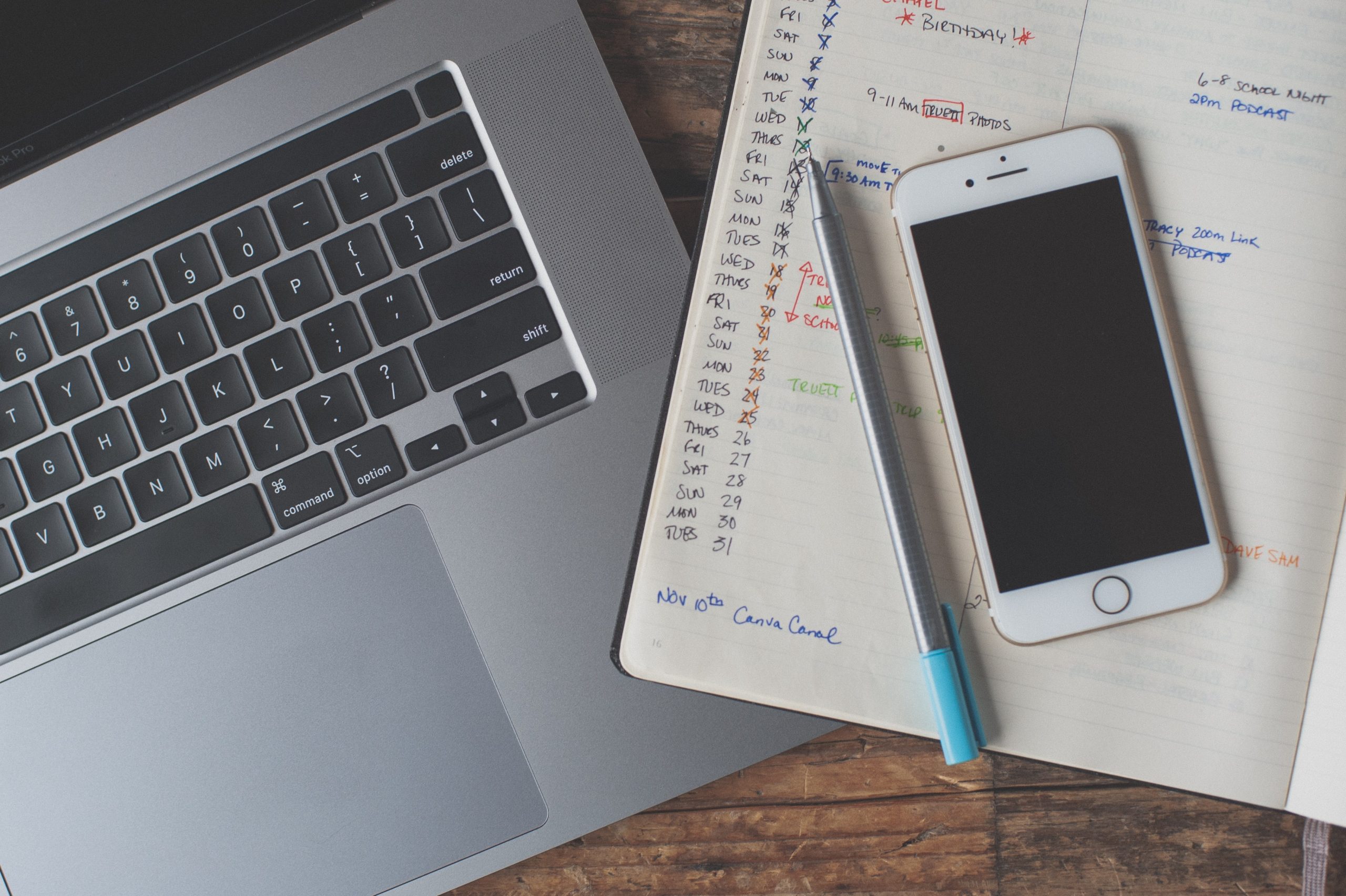 Photo of a white iPhone and blue pen on top of a notebook, next to an iMac