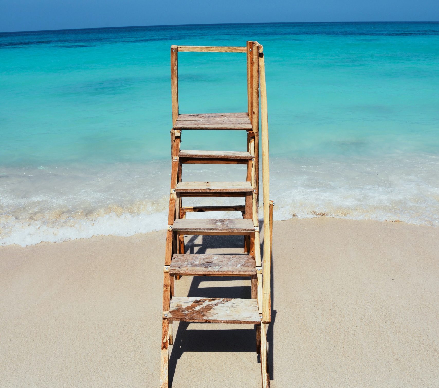 An old wooden stair ladder sits on a sandy beach right at the shore
