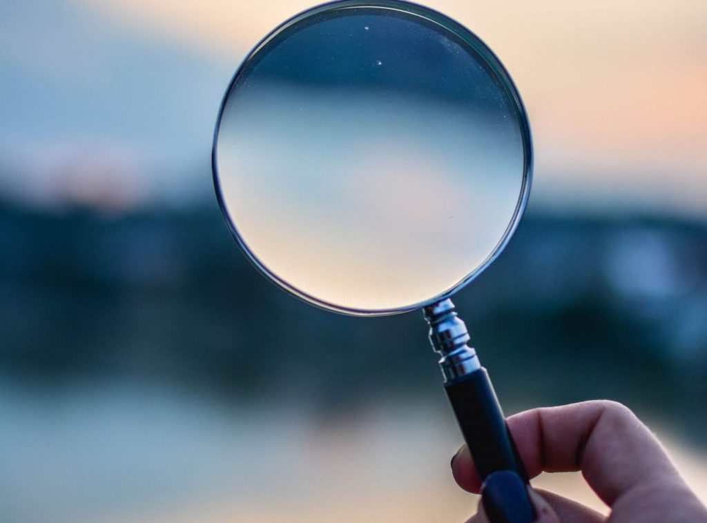 A magnifying glass being held up with a blurred background.