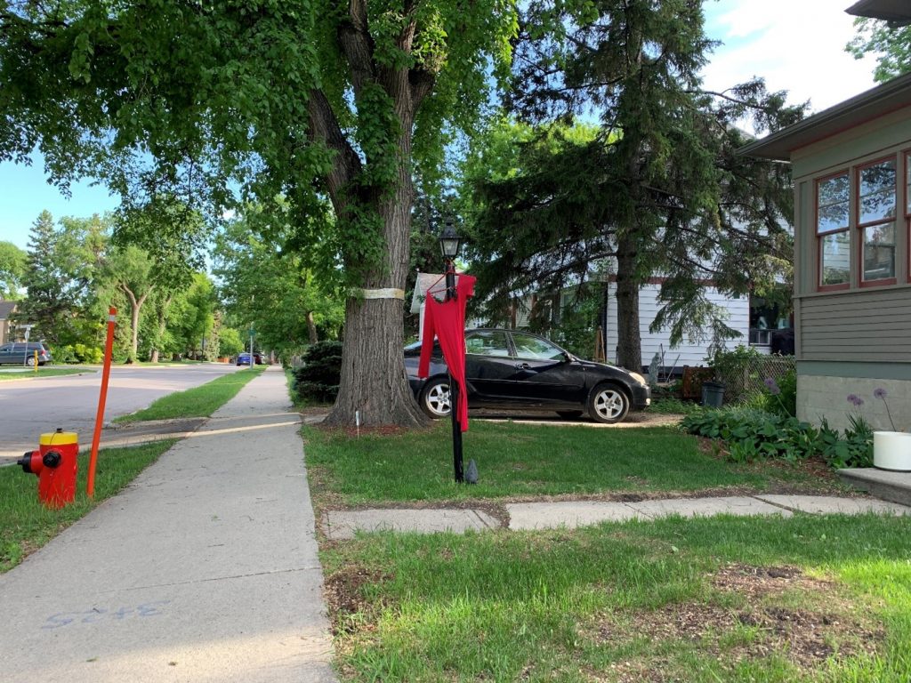 A red dress hangs from a clothes hanger on a lamp post in front a house.