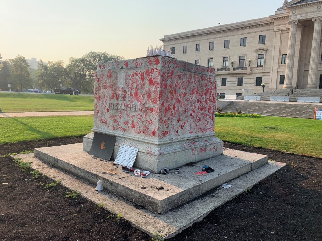 A former statue of Queen Victoria. The statue of the Queen is gone, and the base of the statue is covered in red handprints.