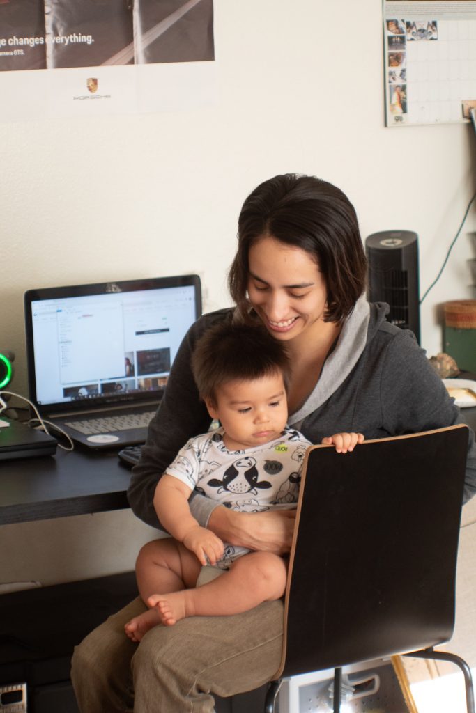 A woman holds a baby on her lap as she tries to work.