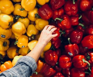 Photo of a hand reaching to touch or select a yellow or red pepper from a very large pile of peppers