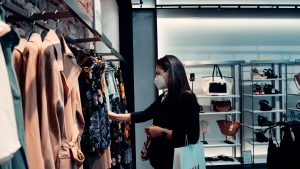 Image of a female shopper in a fashion retail store looking at clothes while wearing a mask.