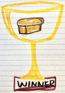 "A ruled piece of white paper with a crude trophy drawn on it. The bowl of the trophy has a picture of a load of bread on it, and the stand has the word 'winner' on it."