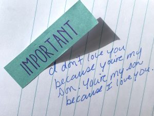 "A rule piece of white paper has a sticky note on it that says 'important.' Under that is handwritten the sentence 'I don't live you because you're my son. You're my son because I love you.'"