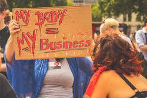 "A person holding up a sign that reads 'my body = my business'"