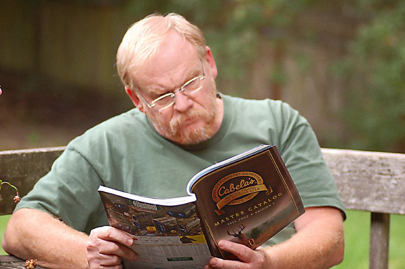 An man reading a Cabela's' catalog outside.