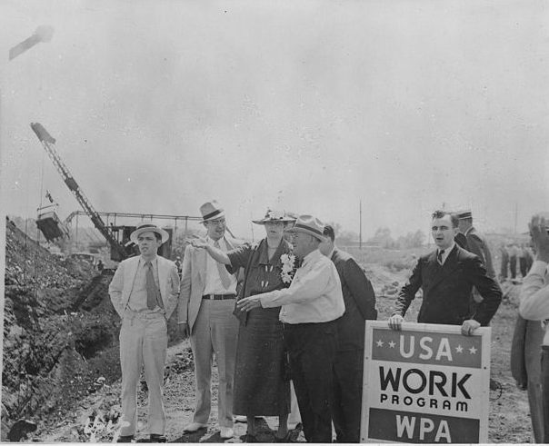 Man holding a USA Work Program sign at Eleanor Roosevelt's side on a construction site.