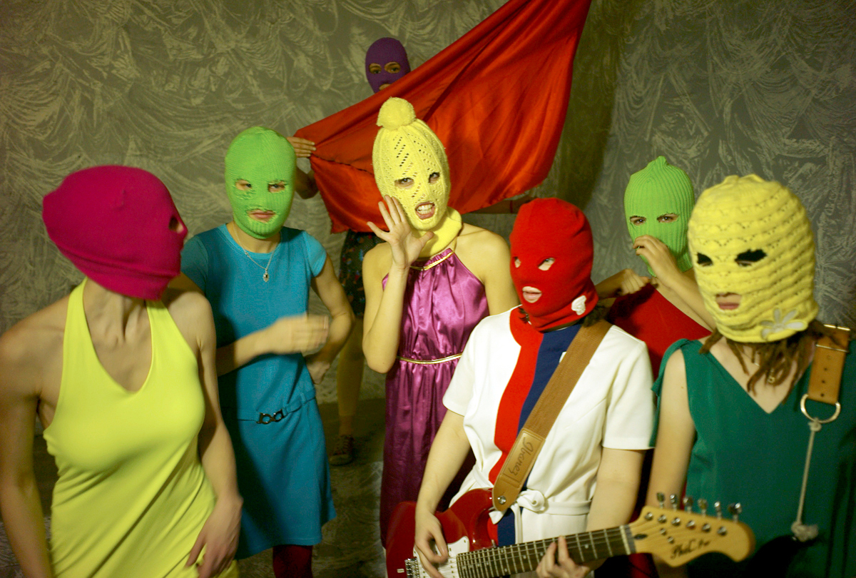 Six women wearing colourful balaclavas, one holding a guitar