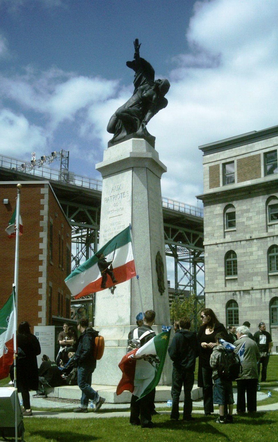 Granite monument surrounded by people with Patriote movement flags.