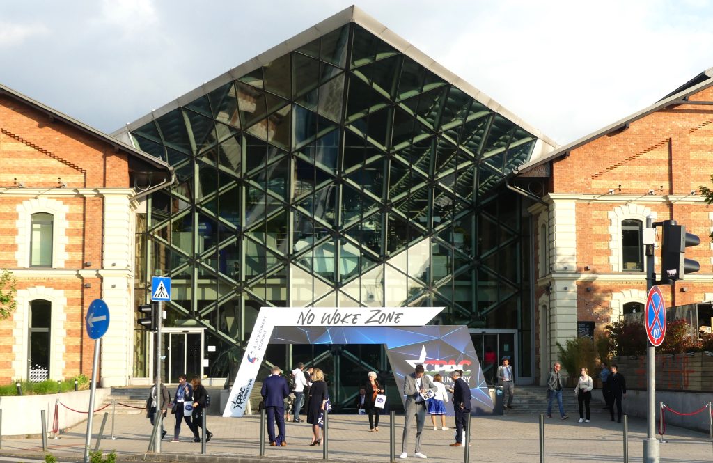 people standing outside a large glass building, a sign on the building reads No Woke Zone