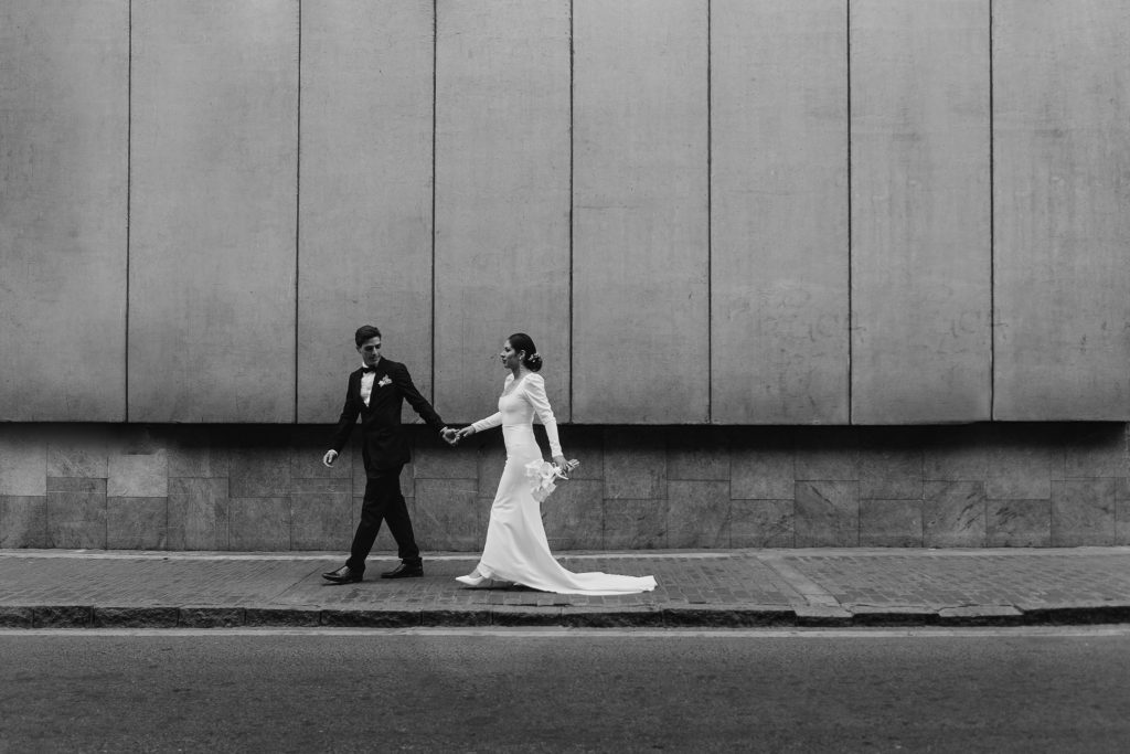 Black and white photo of a bride and groom walking on a sidewalk.