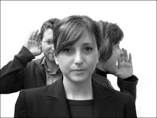 A woman listening as a man listens behind her and a woman speaks to the side of her