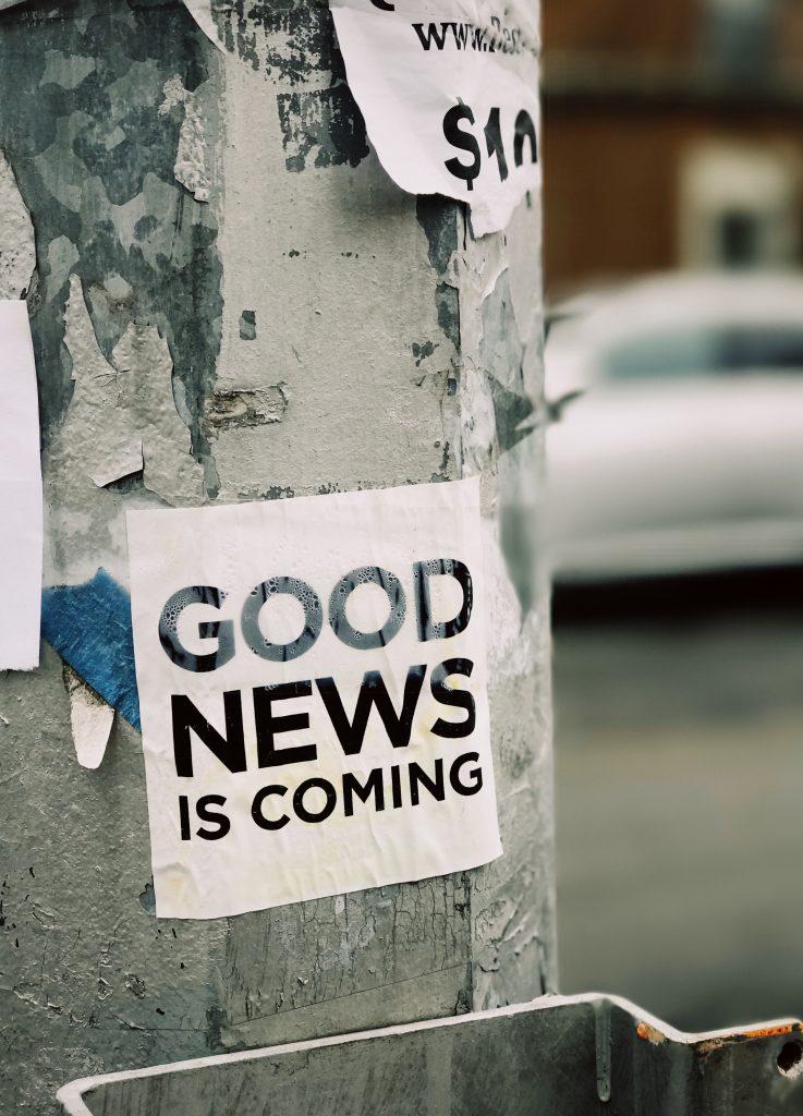 A lamp post with a sticker that reads "Good news is coming."
