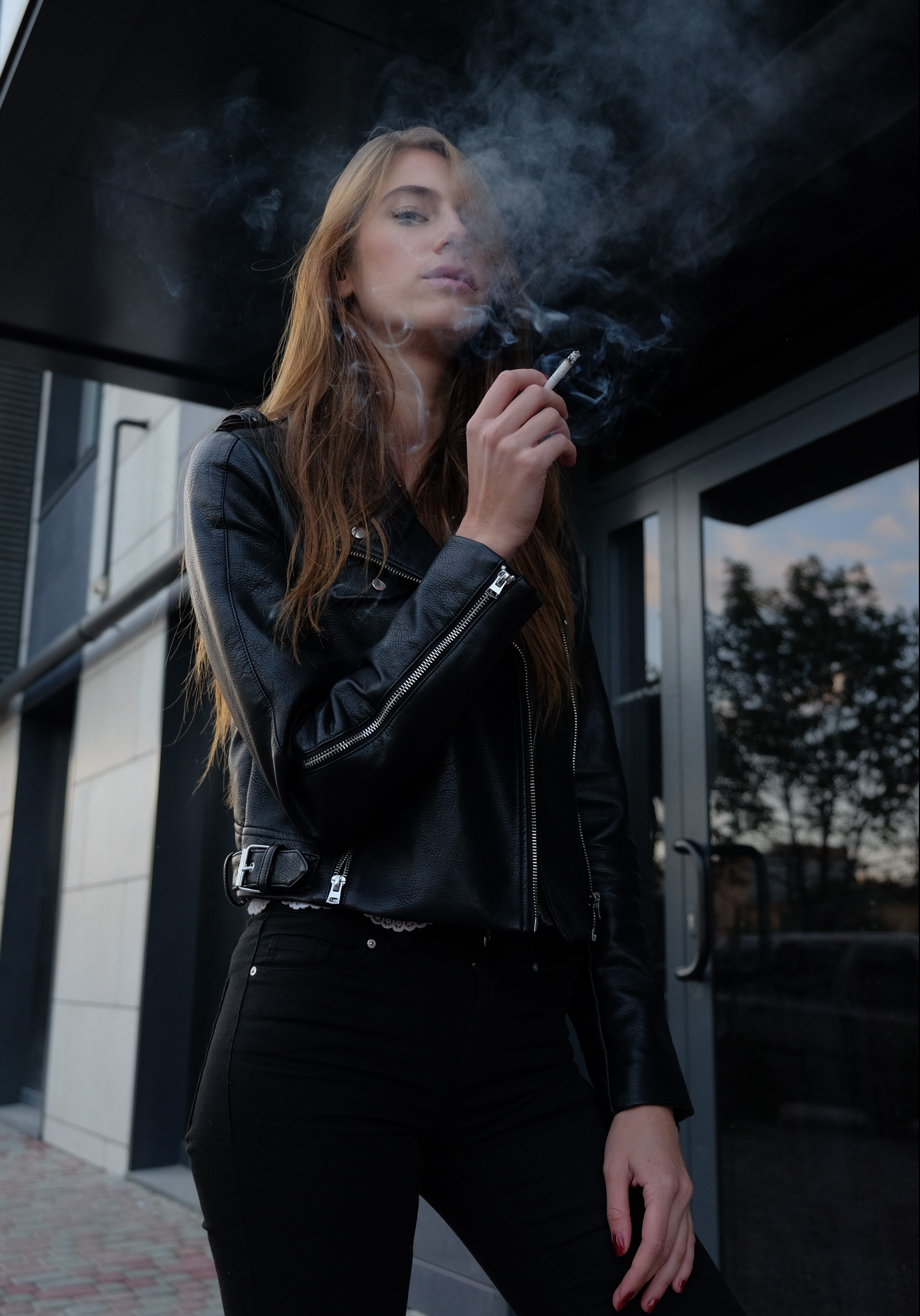 Woman wearing leather jacket smoking a cigarette.
