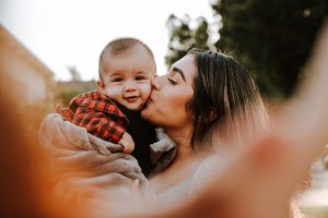 Woman holding and kissing a baby's face cheek.